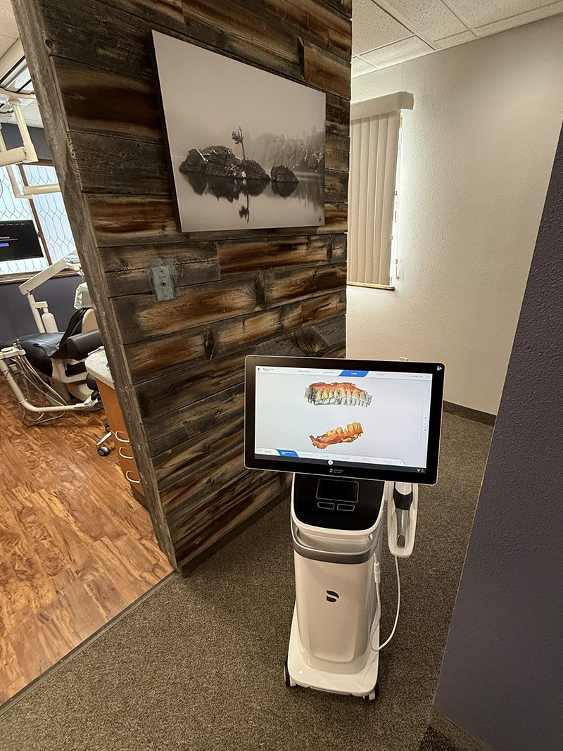 An image featuring a modern dental office with a large screen displaying a digital rendering of teeth, showcasing a dental implant procedure, set against a rustic wall decoration and a framed picture.