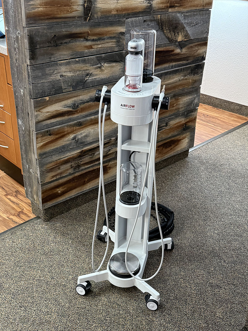 An upright vacuum cleaner on wheels with a transparent dust bag, placed in front of a wall with wooden planks.