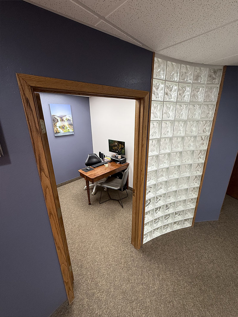 The image depicts an interior office space with a wooden door leading into a room with a desk and a window.