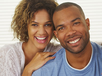 A man and woman posing together with smiles, the man wearing a short beard and the woman with curly hair.